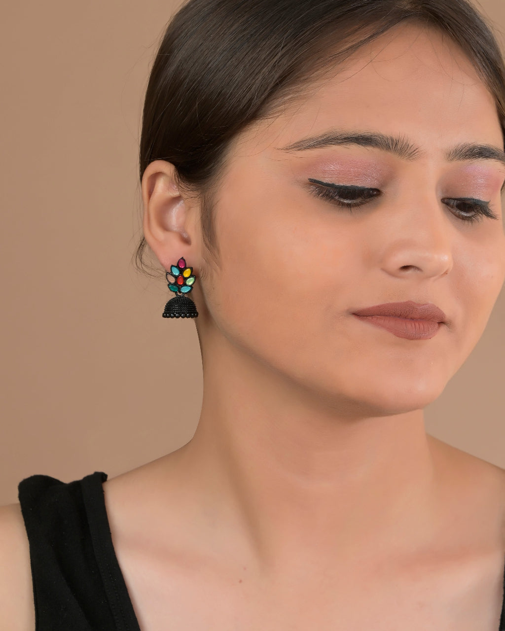 Close-up of a woman wearing colorful tassel earrings against a beige background