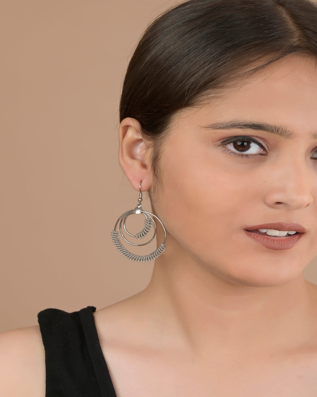 Woman wearing silver hoop earrings against a beige background