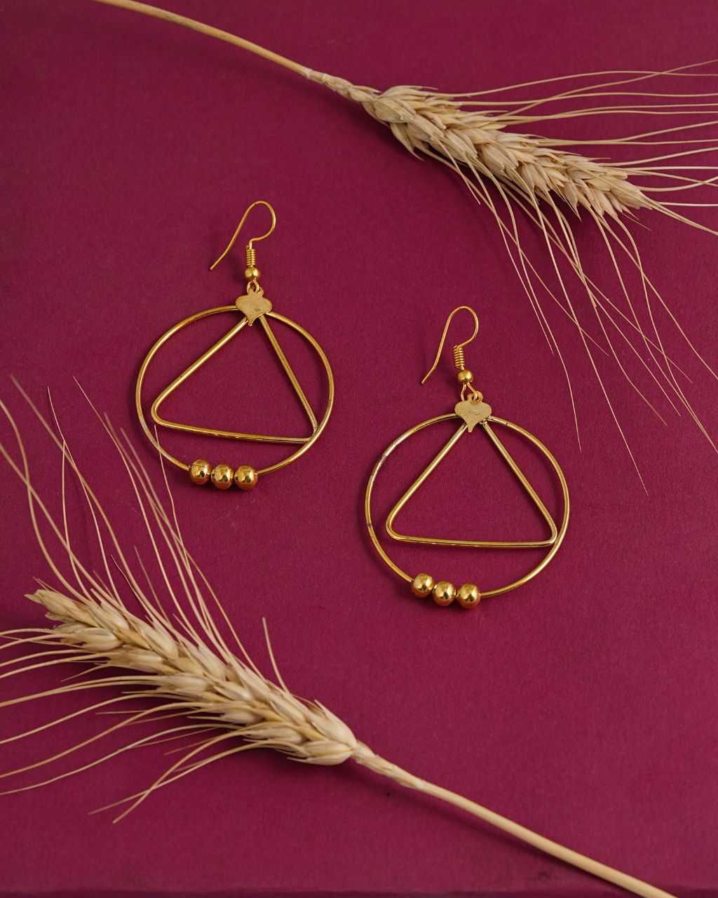 Gold hoop earrings with small beads on a purple background with wheat stalks.