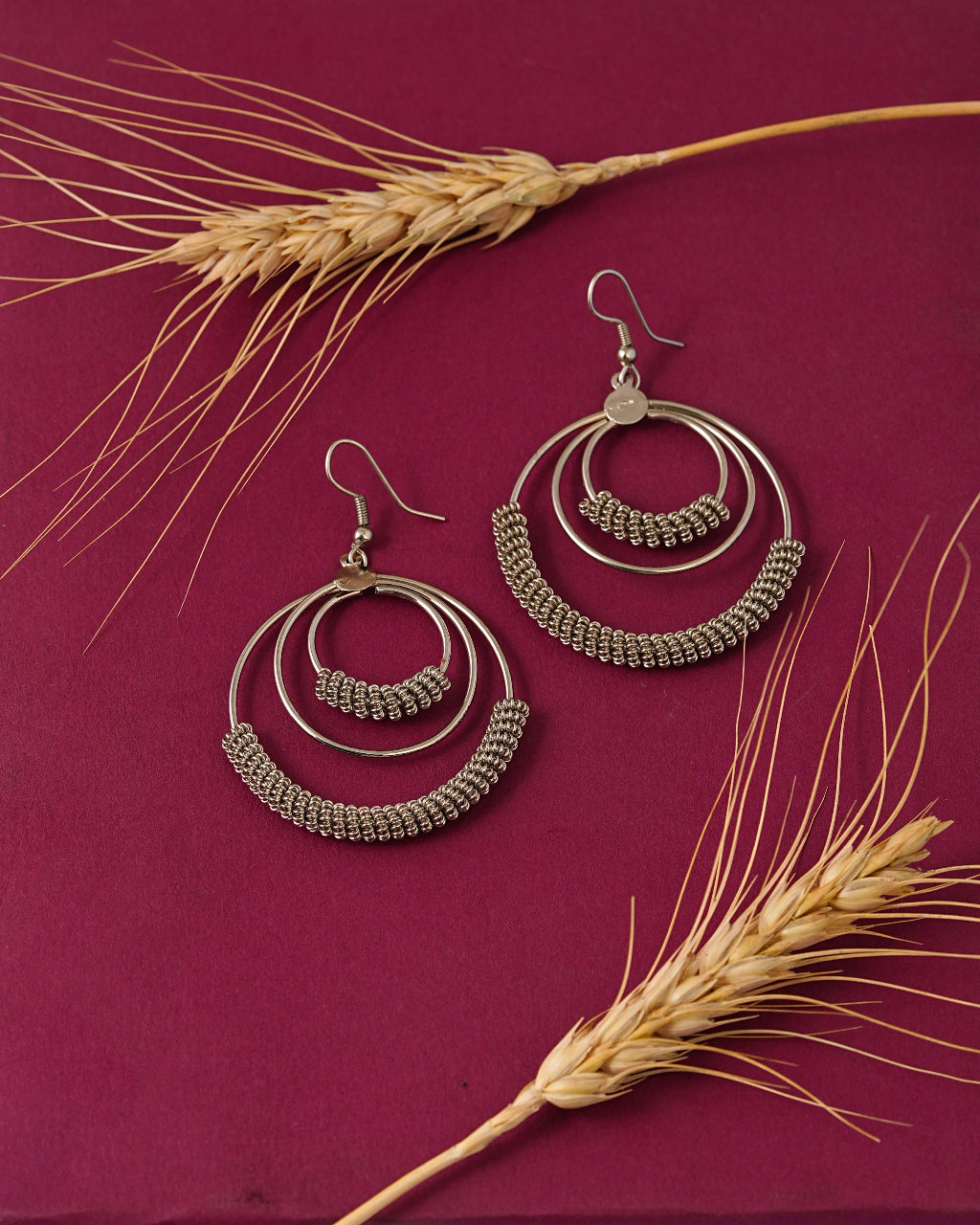Pair of gold hoop earrings on a maroon background with wheat stalks.