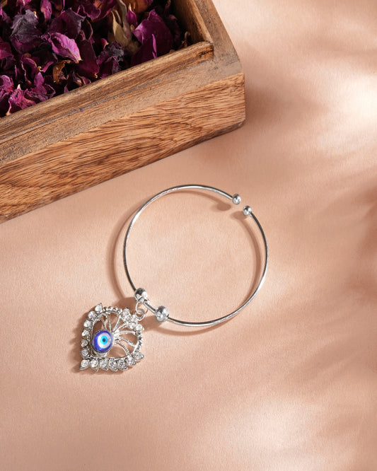 A woman showcases a silver bracelet featuring a heart charm, promoting the Silver Evil Eye Heart Charm Bracelet online.